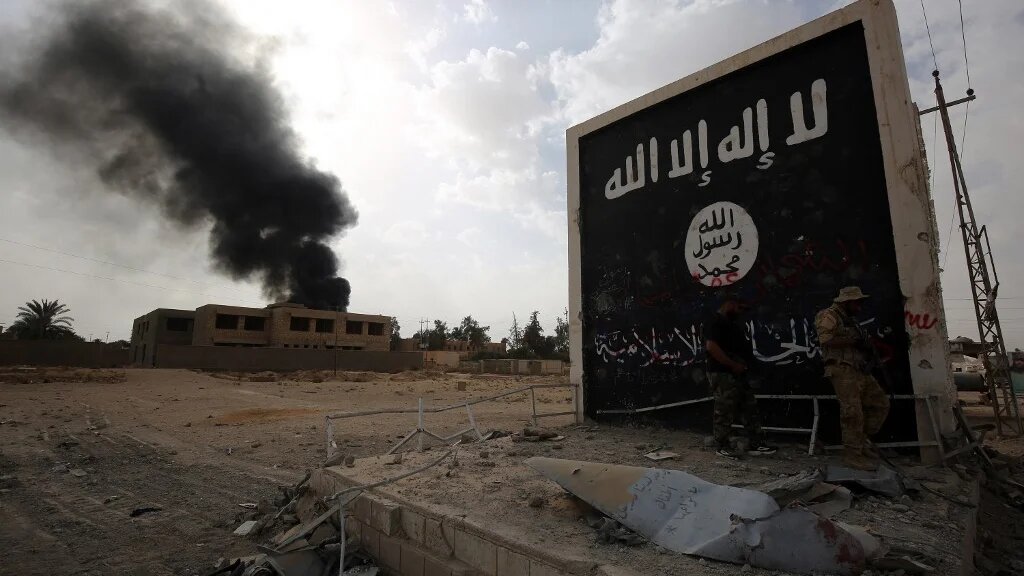 Iraqi fighters stand next to a wall bearing the IS group flag as they entered the city of al-Qaim 
