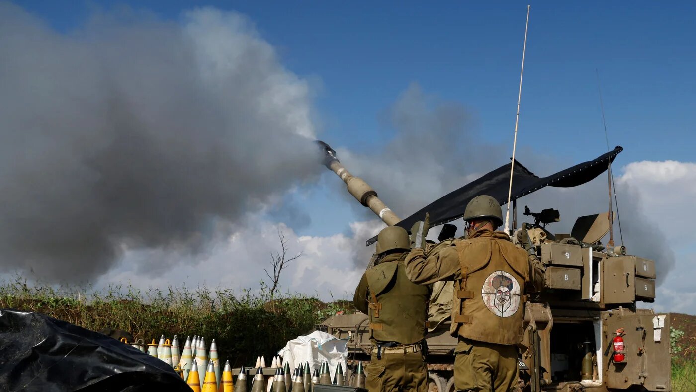 Israeli soldier wearing a patch on the back of his flack jacket showing Lebanon's Hezbollah leader Hassan Nasrallah as a target, stands in front of howitzer in Upper Galilee in northern Israel January 2024, as an artillery unit shells southern Lebanon (Jalaa Marey/AFP)
