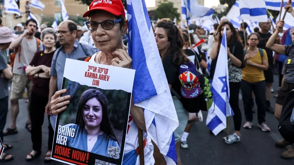 A protester holds a sign identifying Karina Ariev, 19, one of the people taken captive in the Gaza Strip by Palestinian fighters during the 7 October attacks, on 18 June 2024 (AFP)