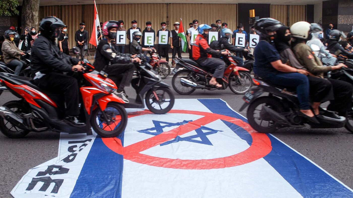 Indonesians place a poster picturing the Israeli flag on the street to be run over by passing vehicles in Bandung, 26 April 2022 (AFP)