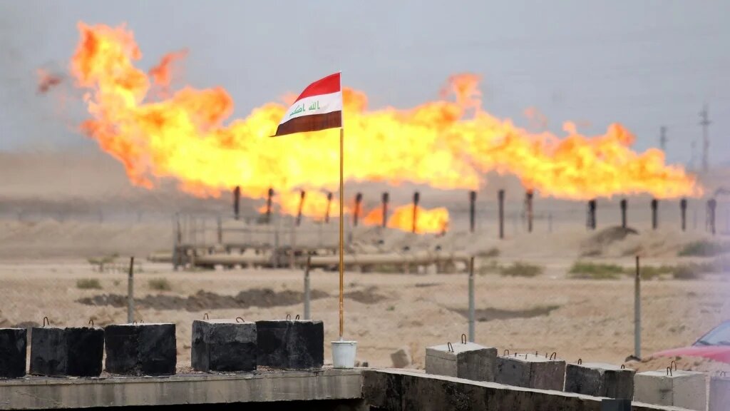 A general view shows an Iraqi national flag flown in front of excess gas as its being burnt off, at a pipeline in the newly opened section of the oil refinery of Zubair, southwest of Basra in southern Iraq, on March 3, 2016 (AFP)