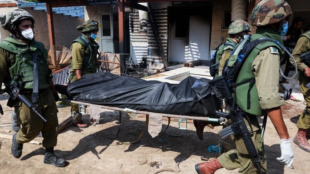 Israeli soldiers remove a body from a house in Kfar Aza on 10 October 2023 (AFP)