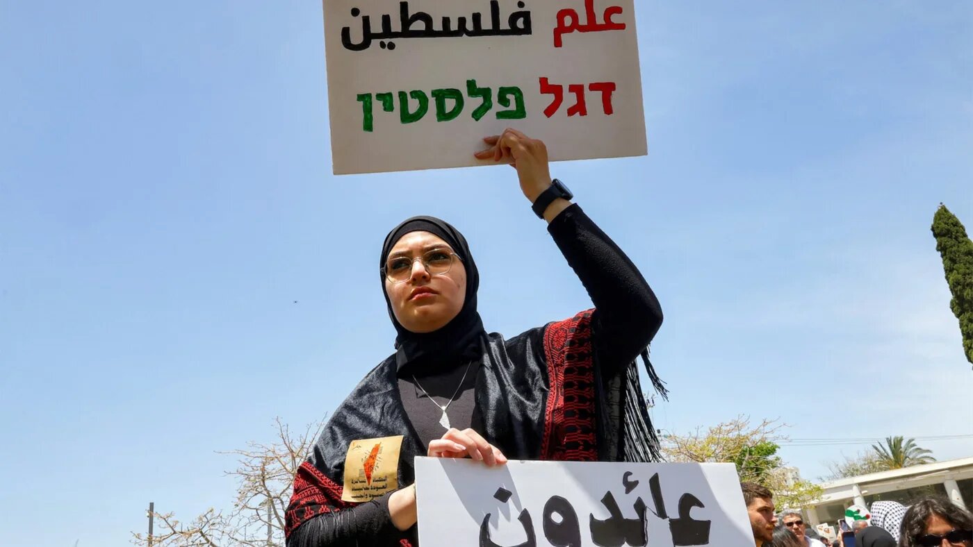 A demonstrator holds Arabic and Hebrew signs saying 'Palestine Flag' and 'Returning' during a Nakba Remembrance Day ceremony at Tel Aviv University on 13 May 2026 (Jack Guez/AFP)