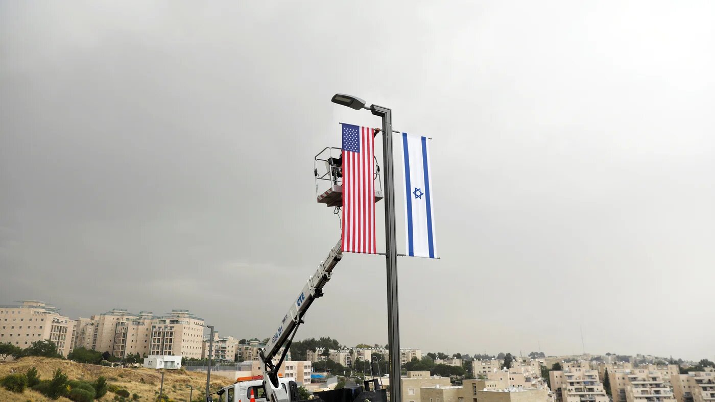 A worker on a crane hangs a US flag next to an Israeli flag, next to the entrance to the US consulate in Jerusalem on 7 May 2018 (Reuters)