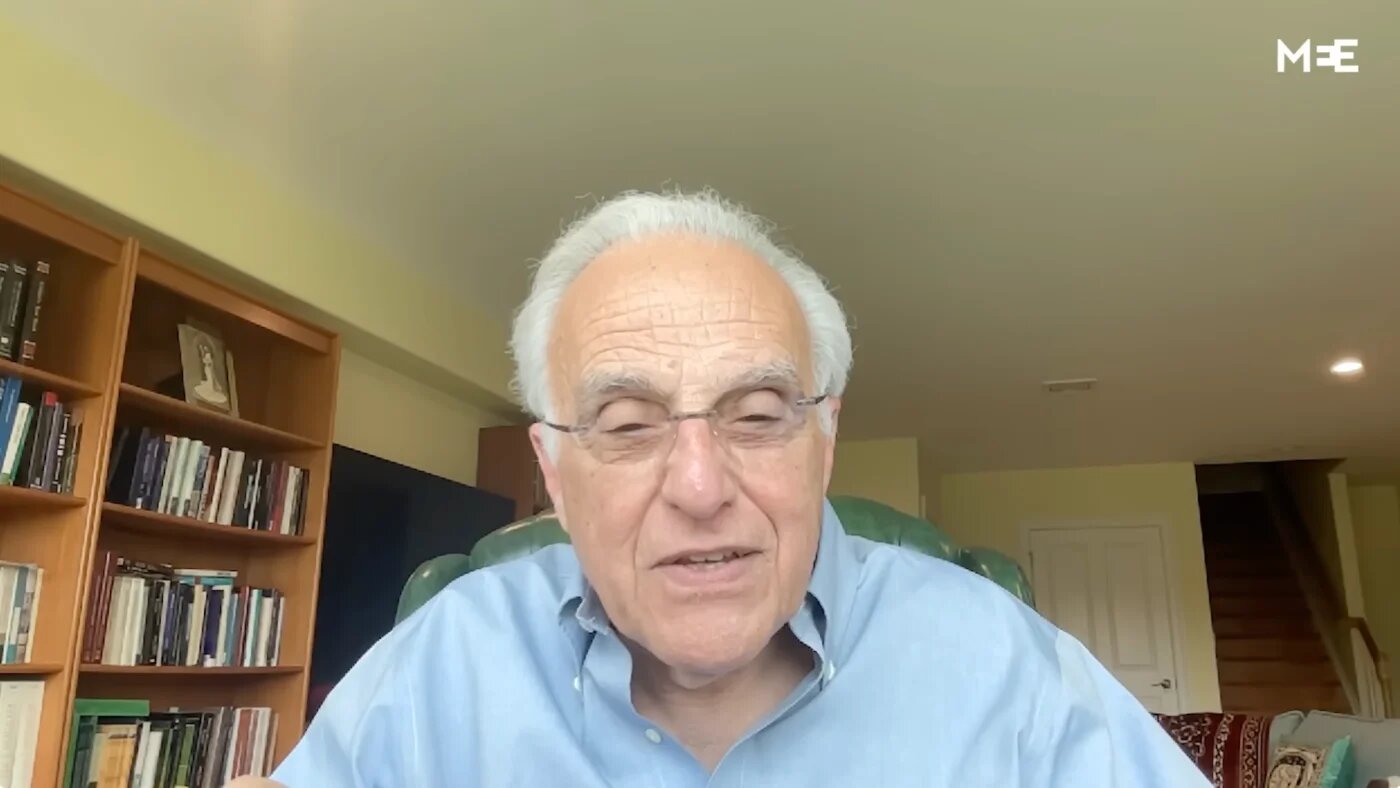 John Esposito smiles during a video interview, bookshelves behind him