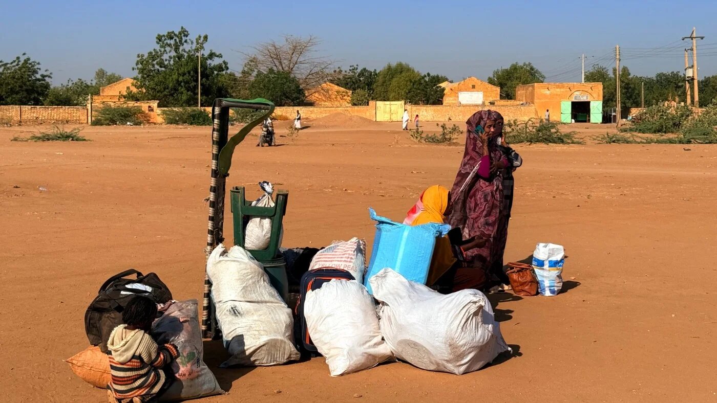 A child and a woman wait next to their belongings as people displaced by the ongoing war in Sudan return to Wad Madani in the Jazira state on 6 February 2025 (AFP)