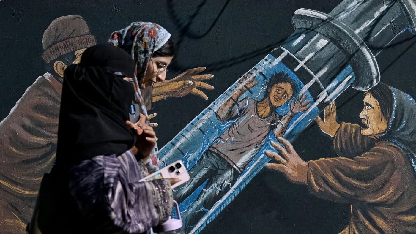 Kashmiri Muslim women walk past a mural in Srinagar, 9 October 2026 (Tauseef Mustafa/AFP)