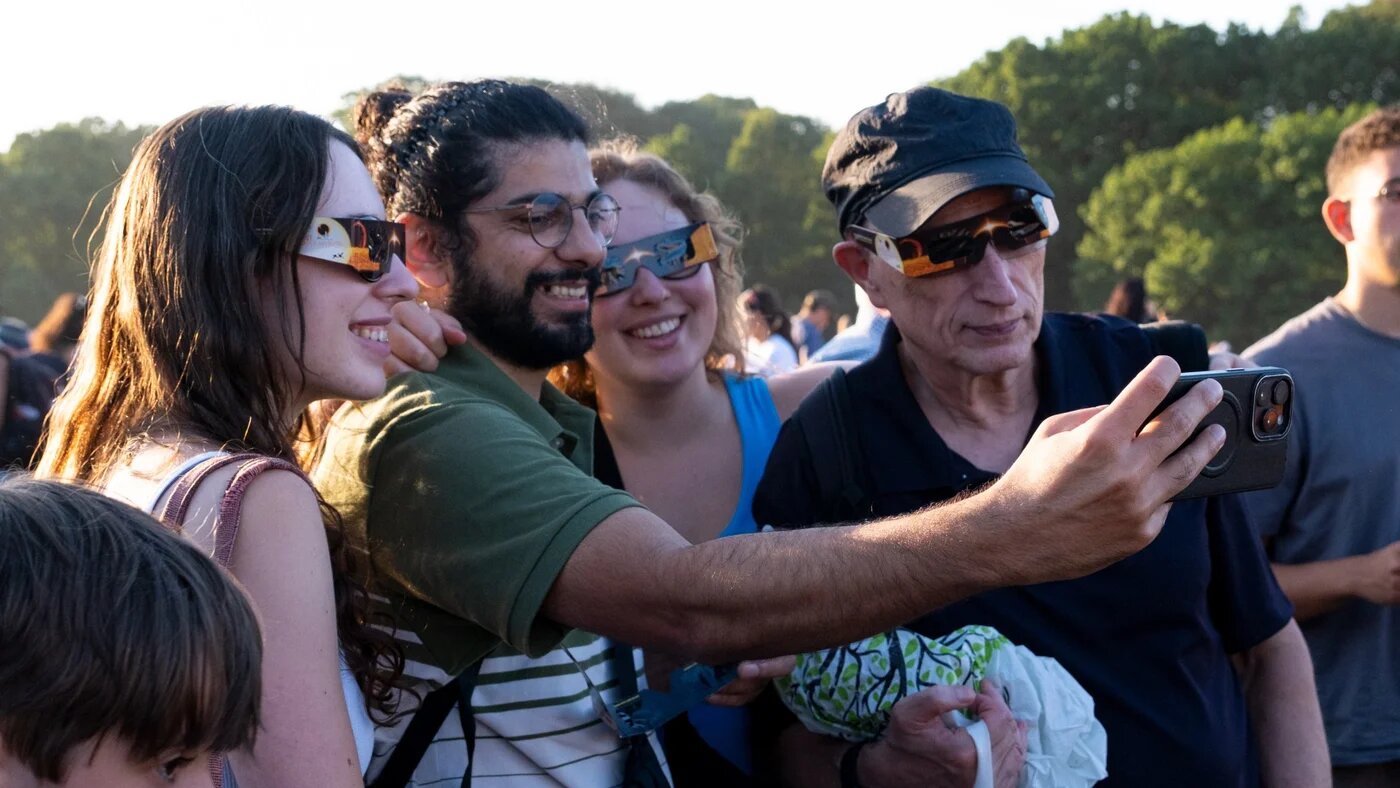 People watch the partial solar eclipse at the Parliament Hill Viewpoint in Hampstead Heath, London. Around a thousand people gathered in the North London park to witness the rare astronomical event. Eclipse-watchers use sheets of paper, colanders, and solar eclipse glasses to view the moon as it passes across the sun. (Photo by Seiya Tanase/NurPhoto)