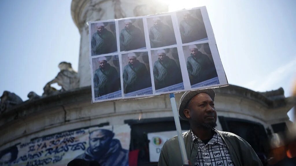A protester holds portraits of Aboubakar Cisse, a worshipper stabbed multiple times in La Grand-Combe on 25 April 2025, in Paris on 1 May 2025 (AFP)