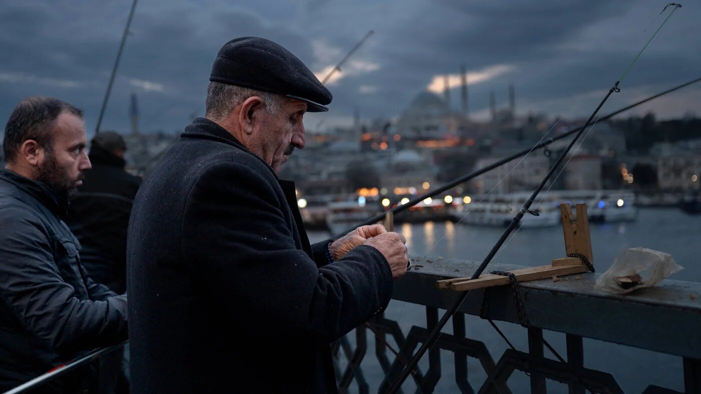 Men stand on the Galata Bridge at sunset fishing not far from the Suleymaniye Mosque, in Istanbul on 7 January 2025 (AFP)