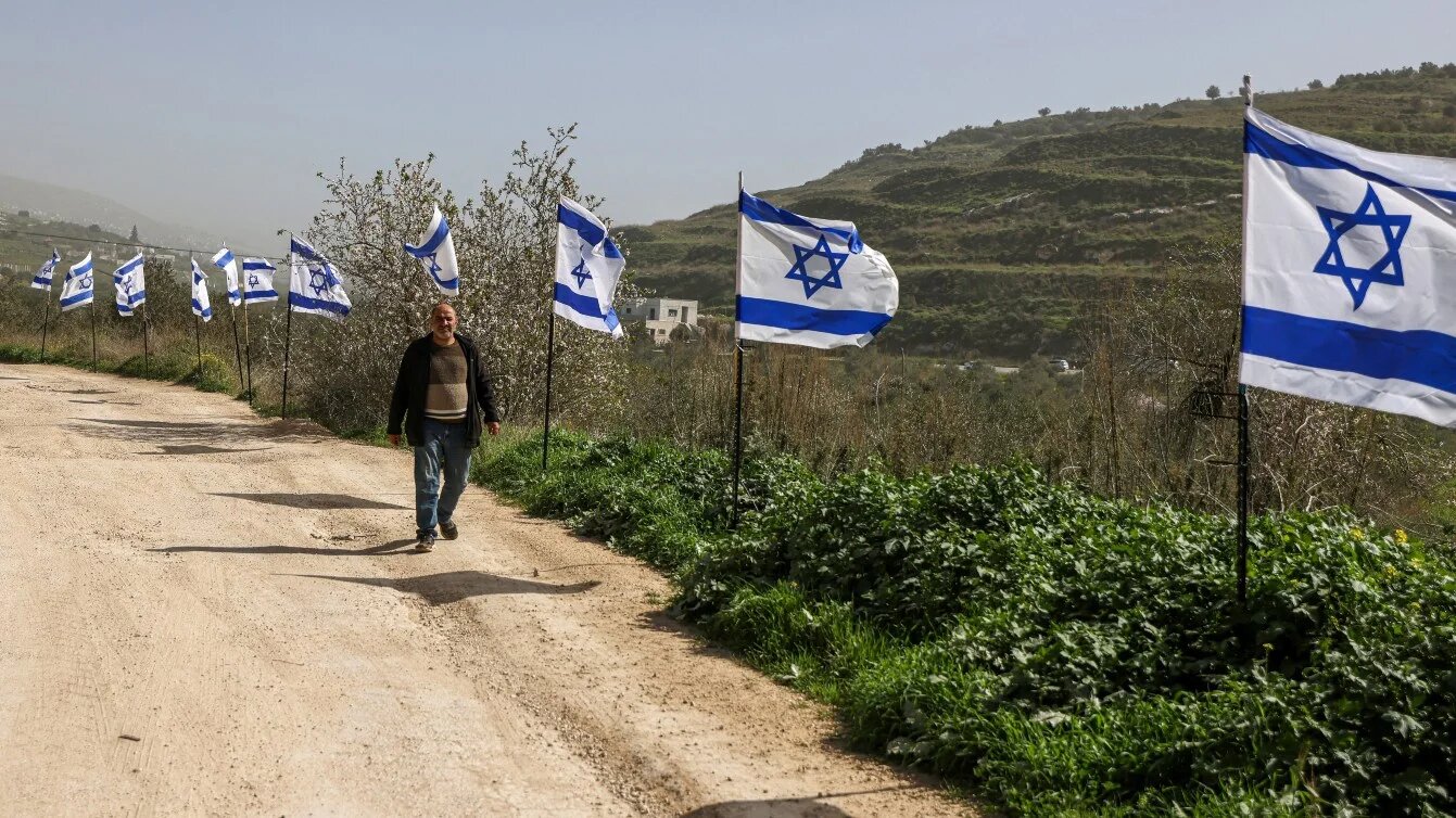 A Palestinian man walks past a fence with Israeli flags installed by Jewish settlers in the northern Israeli-occupied West Bank on 15 February 2026. JAAFAR ASHTIYEH / AFP