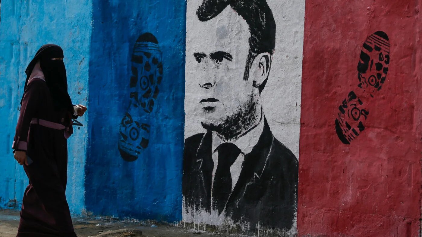 A Palestinian woman walks past a mural bearing the portrait French President Emmanuel Macron in Nuseirat refugee camp in the central Gaza Strip