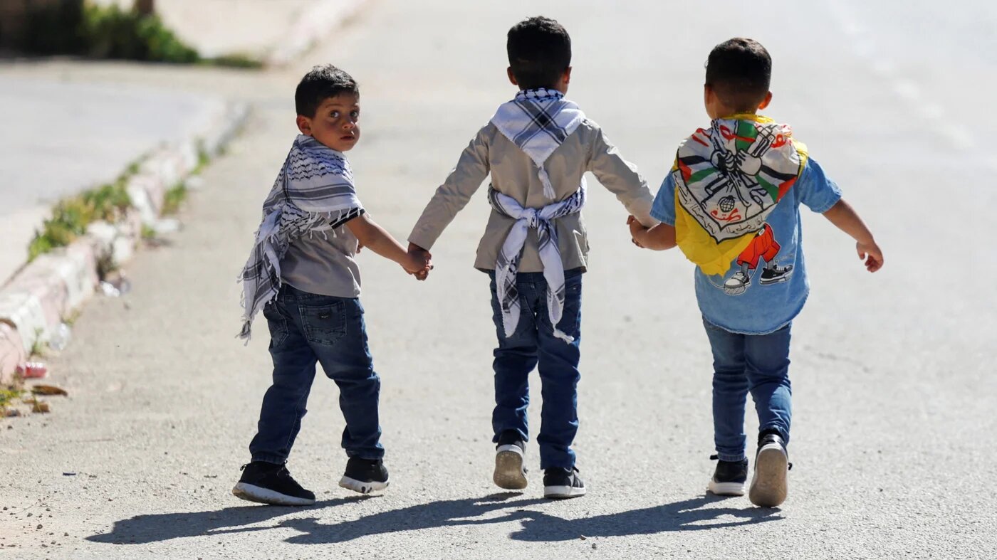 Palestinian children wearing keffiyehs walk along a road in al-Mughayir village near Ramallah, in the Israeli-occupied West Bank, 22 April 2026 (Mohammed Torokman/Reuters)