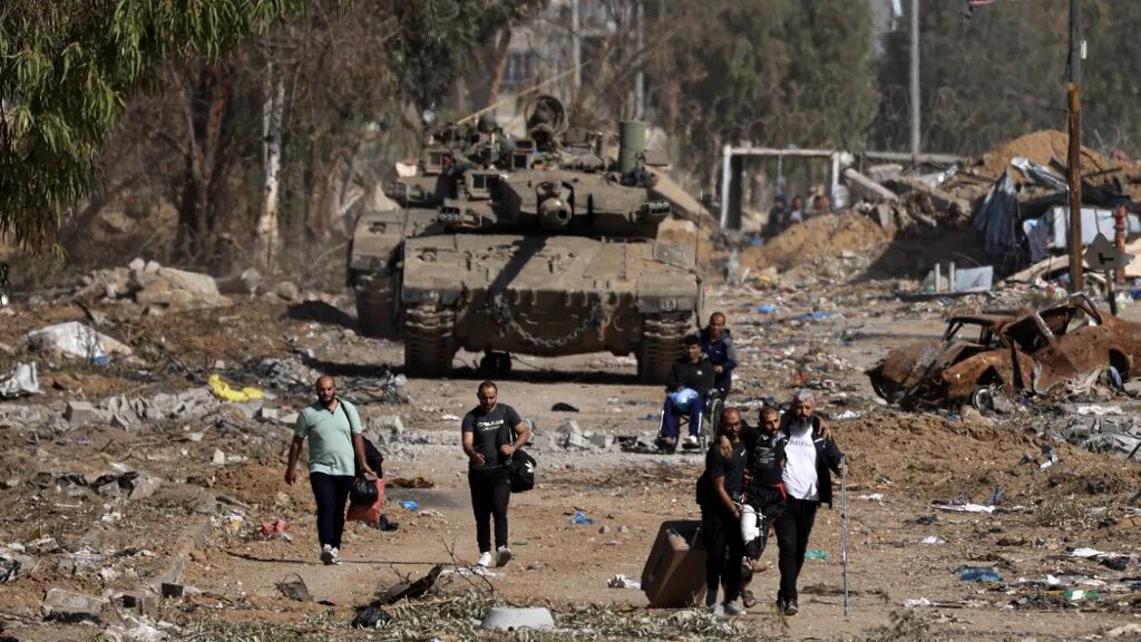 Palestinians fleeing the north through the Salaheddine road in the Zeitoun district on the southern outskirts of Gaza City, walk past Israeli army tanks on November 24, 2023