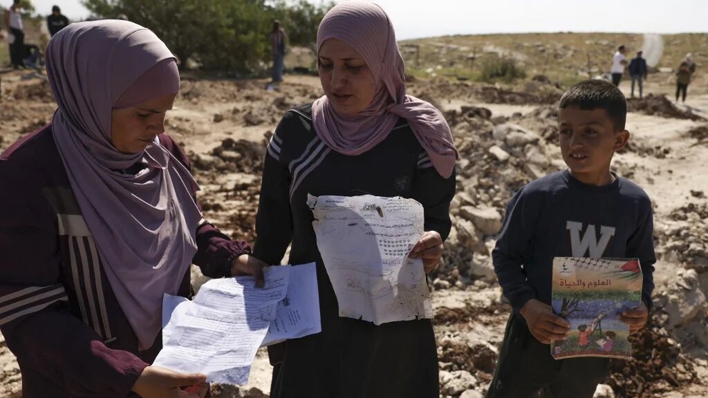 Palestinians pick up papers and books from the site of a school demolished by Israeli authorities in Jabbet al-Dhib, east of Bethlehem in the occupied West Bank, 7 May 2023 (AFP)