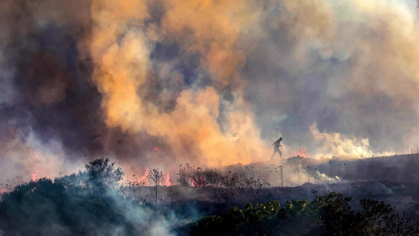 Palestinians walk through smoke from a fire near the village of Tell, west of Nablus in the occupied West Bank, after a reported settler attack, 18 July 2026 (Jaafar Ashtiyeh/AFP)