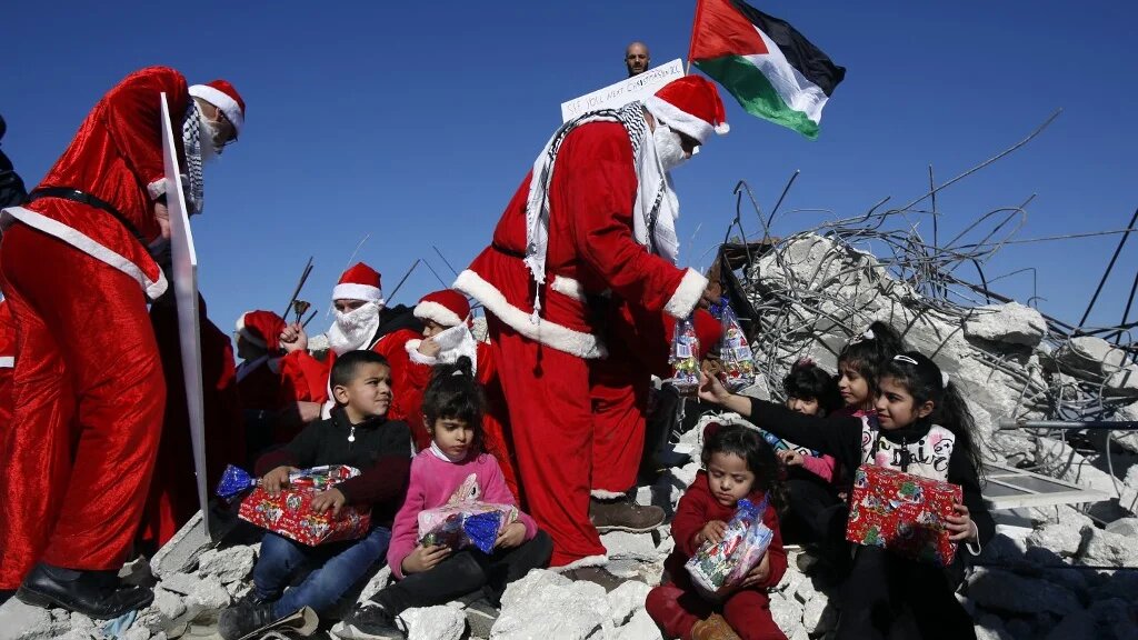 'As ever, one is struck by the sheer resilience of the Palestinian people.' Palestinians wearing Christmas costumes give gifts to children in the rubble of a house in the occupied West Bank demolished by Israel, 23 December 2019 (AFP)
