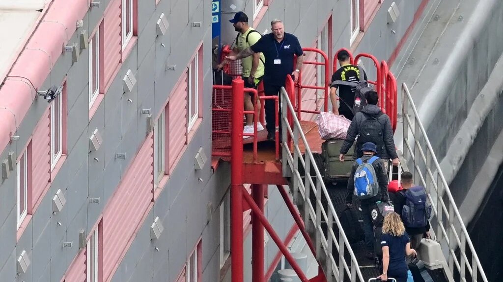 People carrying bags enter the Bibby Stockholm accommodation barge, moored at Portland, Dorset, south-west England, on 7 August 2023 (AFP)