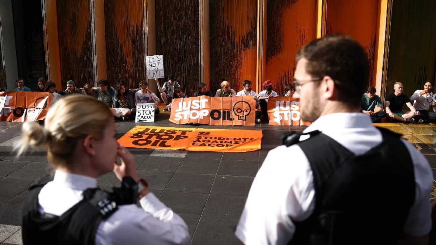 Police officers stand guard as Just Stop Oil climate activists stage a sit-in after throwing orange paint at the UK headquarters of TotalEnergies in the Canary Wharf district in London on 27 June 2023 (AFP)