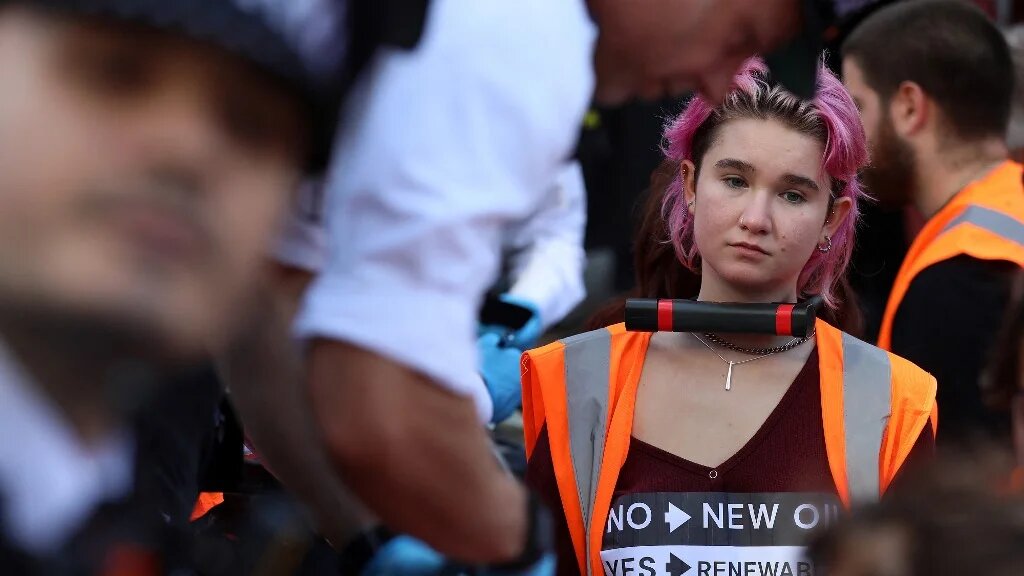 Protesters, with their necks padlocked together, block the road as they take part in a protest by Just Stop Oil climate activists at Piccadilly Circus, London, on 9 October 2022 (AFP)
