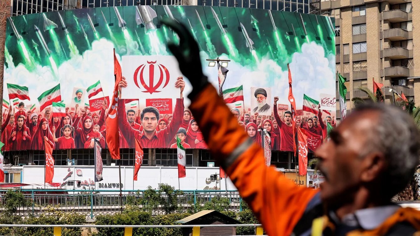 A municipal worker gestures near a large political banner at Valiasr Square in Tehran on 6 April 2026. ATTA KENARE / AFP