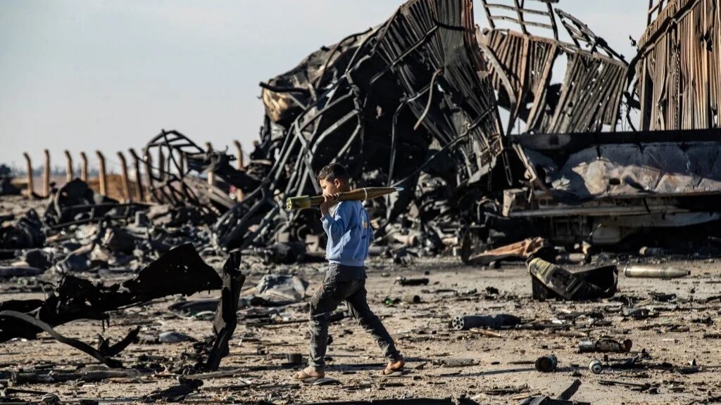 A boy carries an unexploded rocket-propelled grenade (RPG) at the site of an Israeli air strike that targeted shipments of weapons belonging to Syrian government forces in Qamishli, in mainly Kurdish northeastern Syria, on December 10 2024 (Delil Souleiman / AFP)