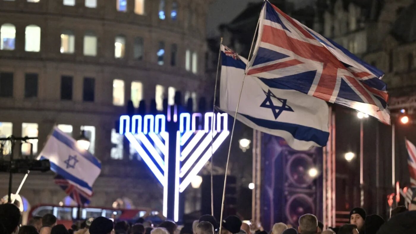 Israeli and British flags are waved as people gather for an event during the Jewish festival of Hanukkah at Trafalgar Square in central London on 16 December 2025 (AFP/Richard A Brooks)