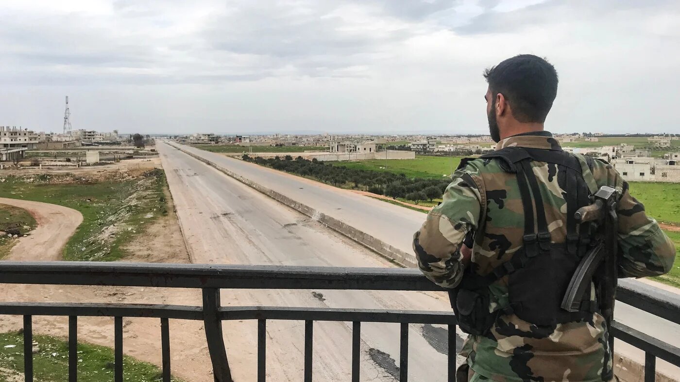 A Syrian army soldier stands overlooking a motorway 