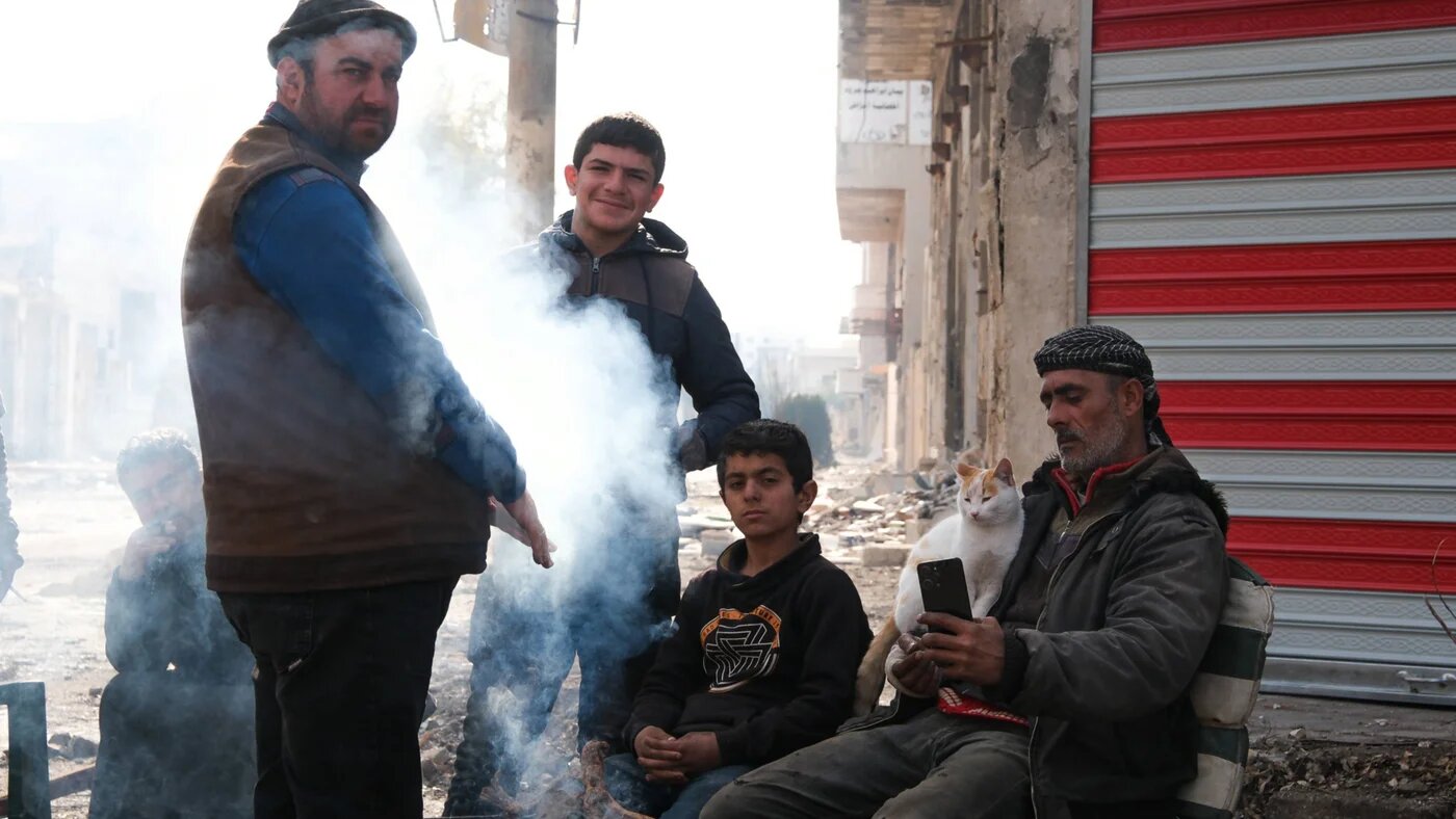 Syrians who have returned to Saraqib to reclaim their homes warm themselves on a brazier in the centre of town, 31 December 2024 (Andrew Waller/MEE)  