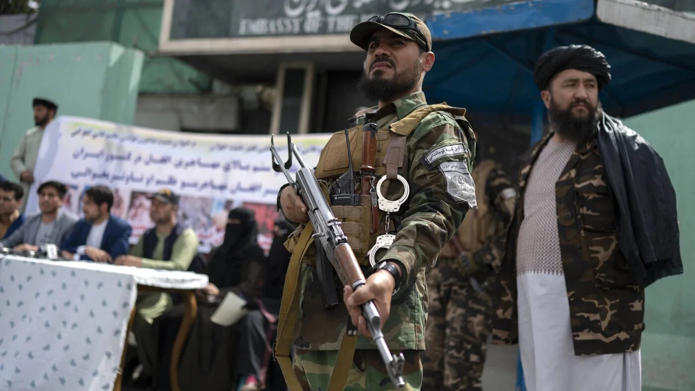 Taliban fighters stand guard as Afghan protesters take part in a demonstration against reports of harassment of Afghan refugees in Iran, in front of the Iranian embassy in Kabul on 11 April 2022