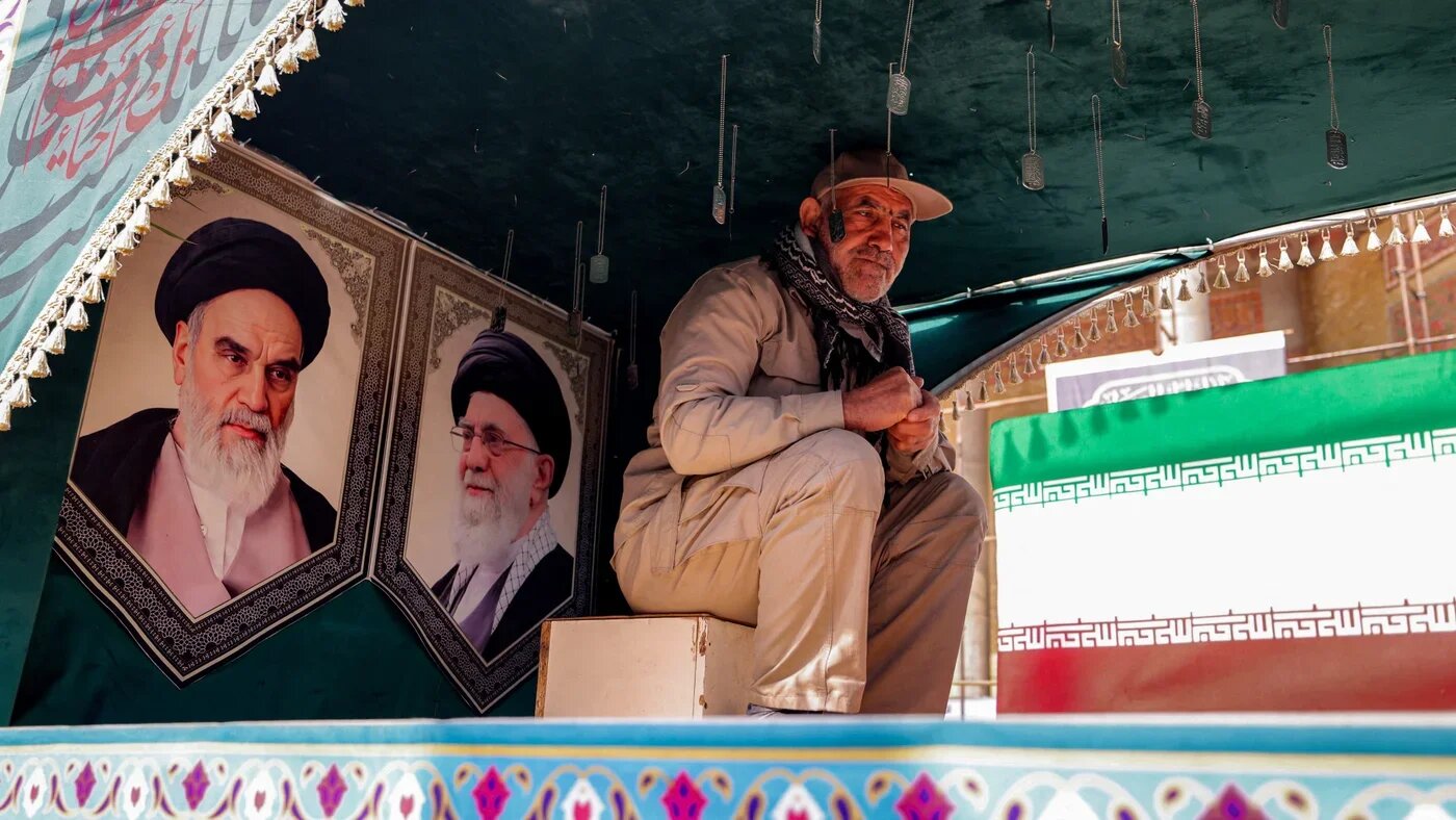A man sits beside portraits of Ayatollah Ruhollah Khomeini and Ayatollah Ali Khamenei during a burial ceremony for a person killed in recent US-Israeli strikes, in Tehran on 9 March 2026 (Atta Kenare/AFP)
