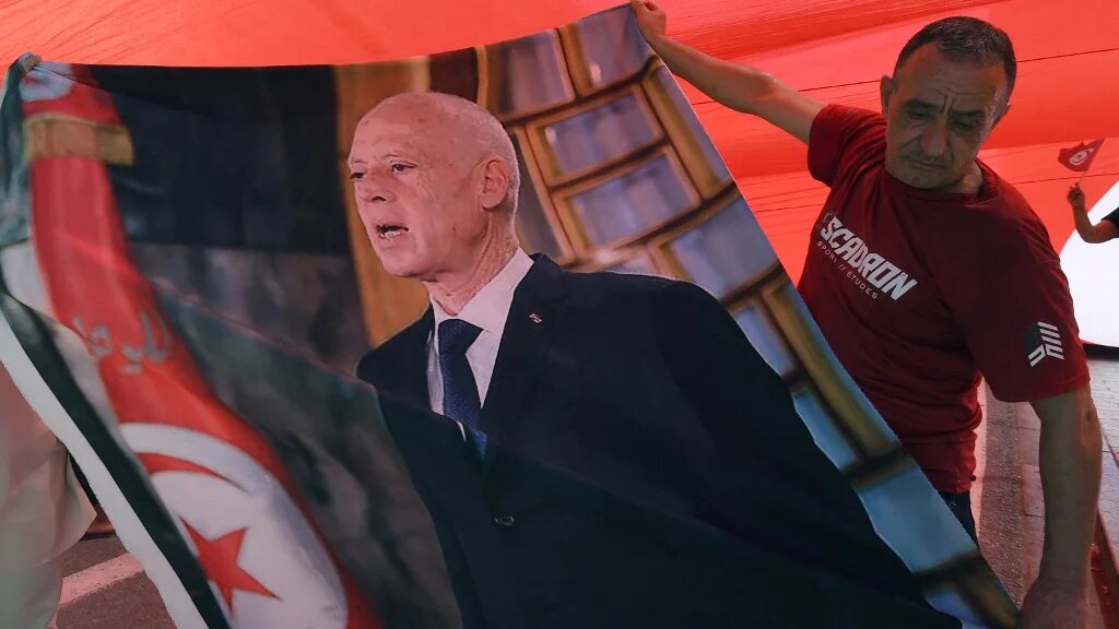 A supporter of President Kais Saied hold his image as he stands under a national flag during a rally in Tunis on 25 July (Fethi Belaid/AFP)