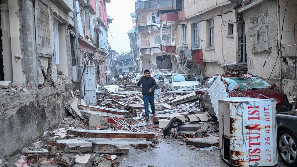 A man runs along a street strewn with debris, in Hatay, southern Turkey, on 7 February, 2023 (AFP)