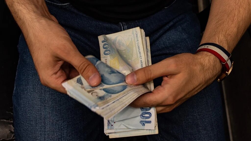 A currency exchange office worker counts Turkish Lira banknotes in front of the electronic panel displaying currency exchange rates at an exchange office in Istanbul, on August 6, 2020  (Yasin Akgul / AFP)