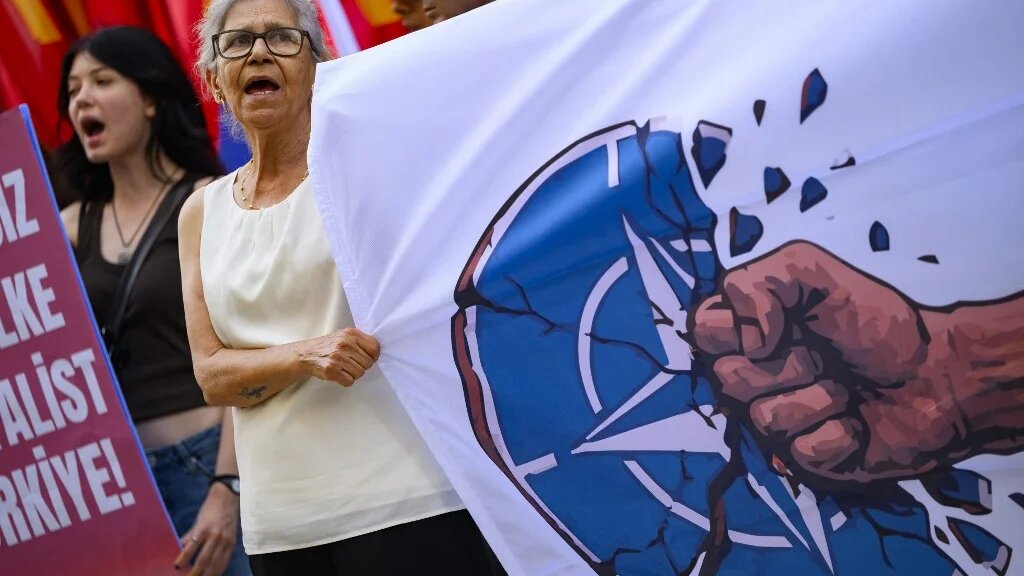 A protestor hold a banner bearing the NATO logo being destructed by a punch during an anti-NATO demonstration in Istanbul, ahead of a NATO summit, on July 5, 2026. The next NATO summit will take place in Ankara on July 7-8 and is expected to be attended by 32 leaders including US President. (Yasin AKGUL / AFP)