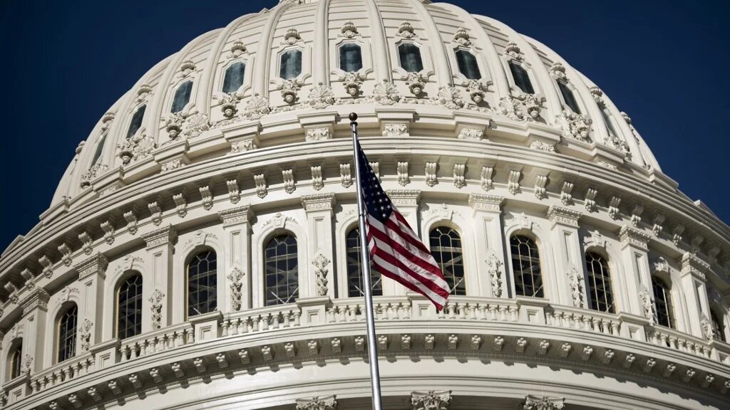 A US flag waves in front of the US Capitol building.