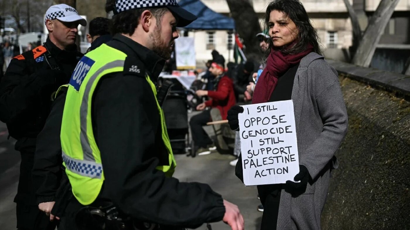 Police confront Ams, who holds a sign reading "I still oppose genocide, I still support Palestine action" in central London on 15 March 2026 (AFP)