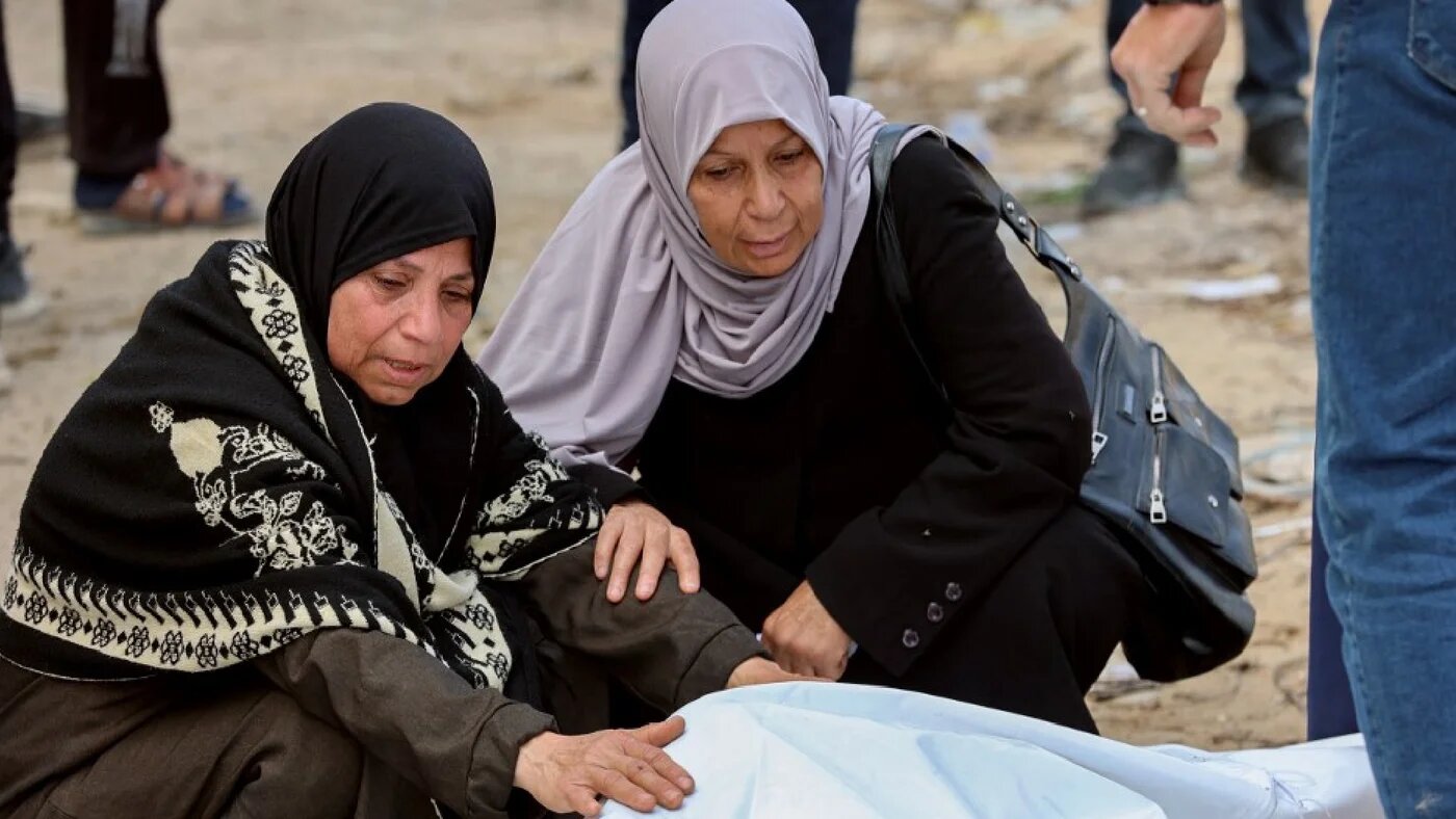 Women mourn over a body after Palestinian civil defence workers uncovered corpses buried in the grounds of Al-Shifa hospital in Gaza City, on March 13, 2025 (AFP)