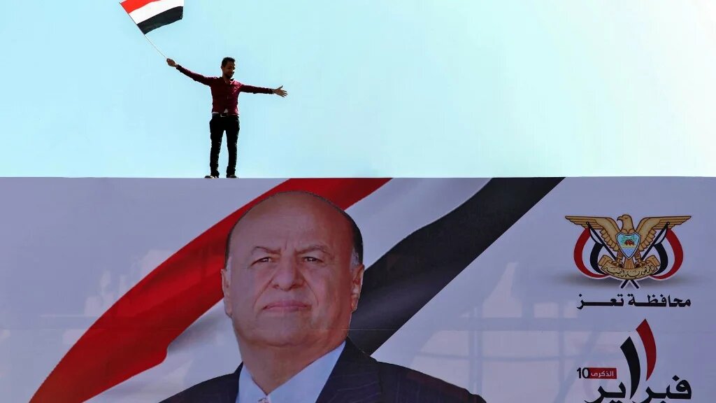 A Yemeni waves the country's national flag on a billboard showing President Abd Rabbuh Mansour Hadi 