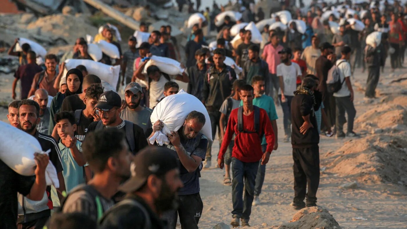 People carrying sacks of flour walk along al-Rashid street in western Jabalia on 17 June 2025 (AFP/Bashar Taleb)