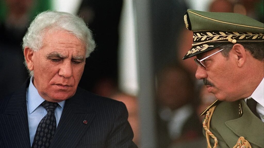 Le général Khaled Nezzar (à droite) et le président algérien Chadli Bendjedid – lui aussi accusé, mais à tort, d’avoir fait partie de l’armée française –, à l’occasion du 35e anniversaire du déclenchement de la révolution algérienne de 1954, le 1er novembre 1989 à Alger (AFP)