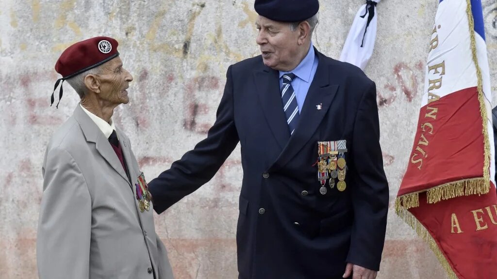 Deux harkis assistent à un rassemblement des harkis au camp de Rivesaltes pour alerter les politiques sur une loi de réparation, à l’occasion de la journée nationale de commémoration et de réflexion à la mémoire des victimes civiles et militaires de la guerre d’Algérie, soixante ans après la signature des accords d’Évian à Salses-le-Château, dans le sud de la France, le 19 mars 2019 (AFP/Raymond Roig)