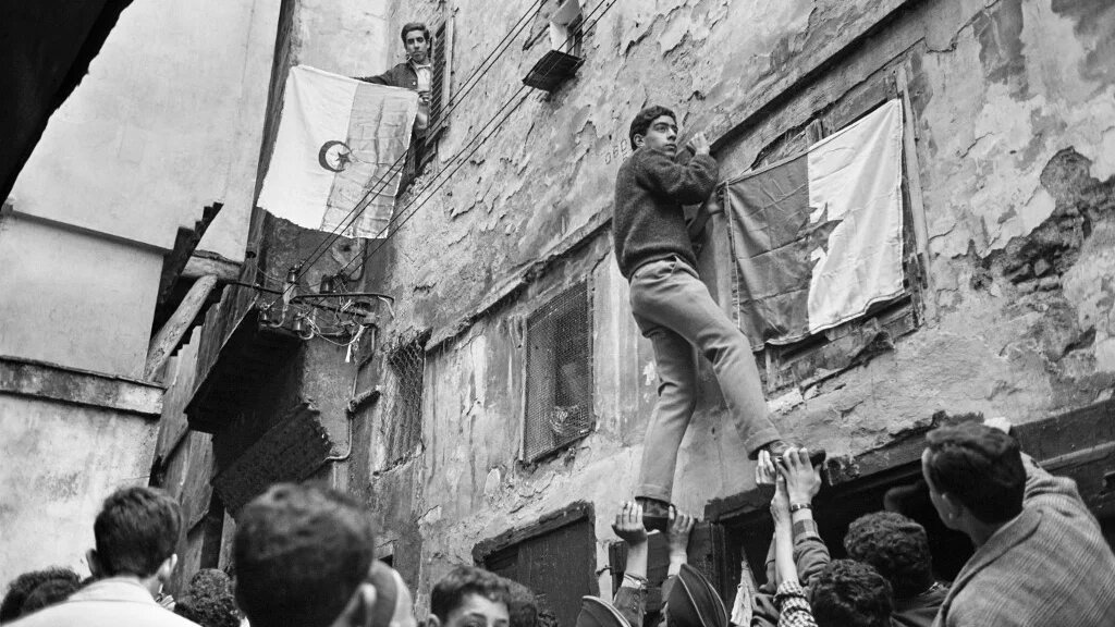 De jeunes Algériens accrochent un drapeau national sur un mur de la Casbah d’Alger, le 6 juillet 1962, au lendemain de la proclamation de l’indépendance (AFP)