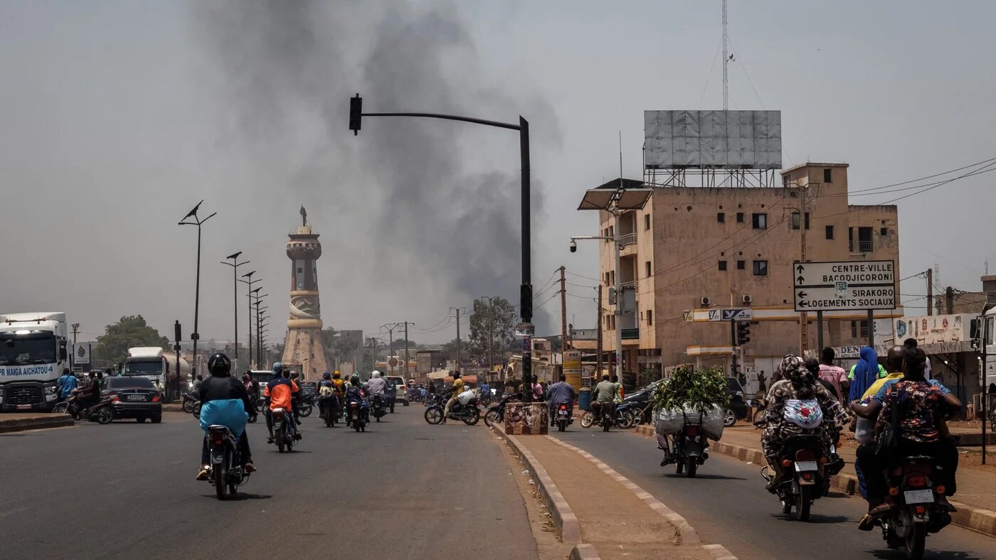 A column of black smoke rises above buildings as traffic passes the Africa Tower monument in Bamako on 26 April 2026 (AFP)