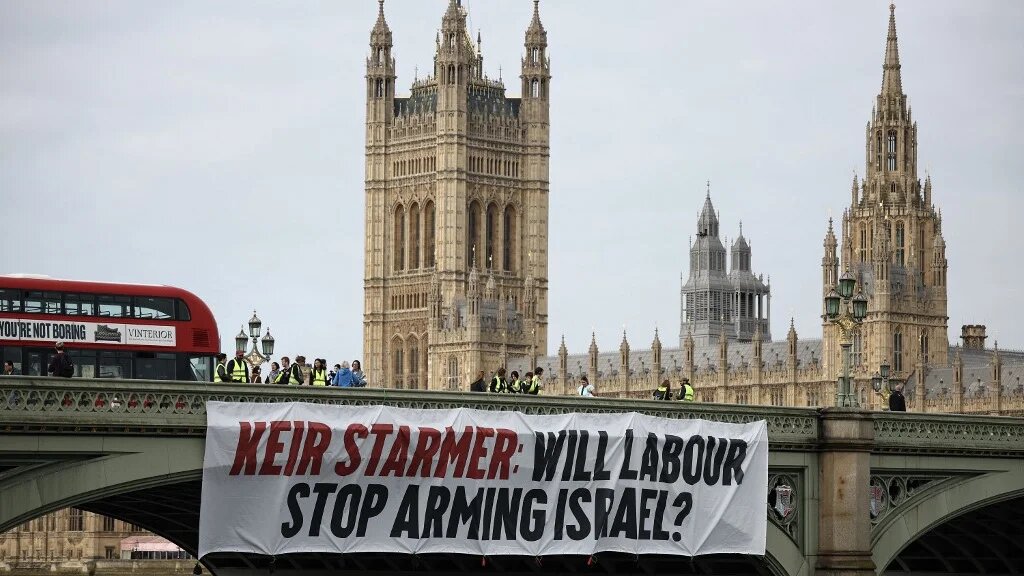 A banner reading 'Keir Starmer: Will Labour Stop Arming Israel?' is hung over the side of Westminster Bridge, in front of the UK parliament, London, 3 June 2024 (Henry Nicholls/AFP)