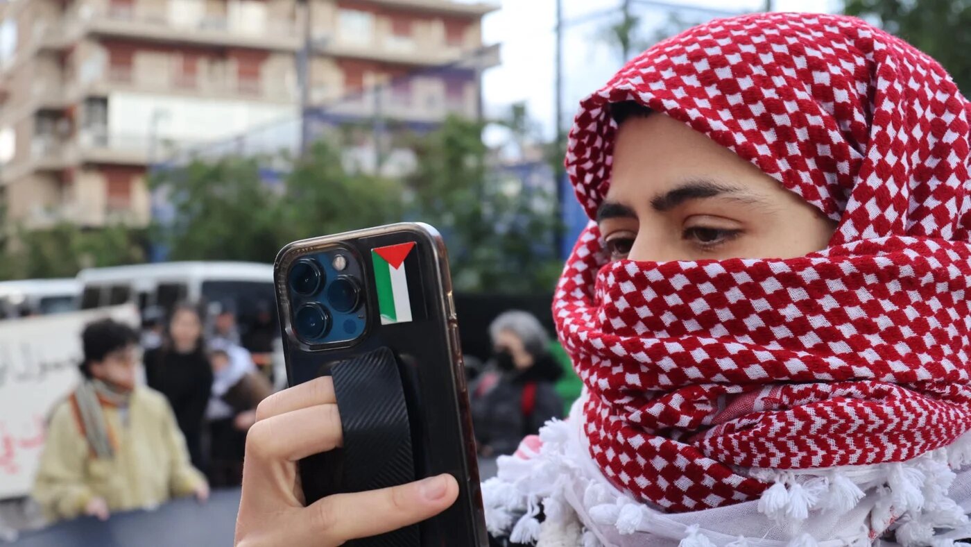 An activist wearing a chequered keffiyeh takes pictures with a smart phone bearing a Palestinian flag sticker as demonstrators block the road leading to the Egyptian embassy in the Lebanese capital Beirut in protest against the closure of the Rafah crossing between Egypt and the Gaza Strip, on February 19, 2024. Egypt, which controls the Rafah border crossing, has repeatedly warned against any "forced displacement" of Palestinians from Gaza into the Sinai desert.