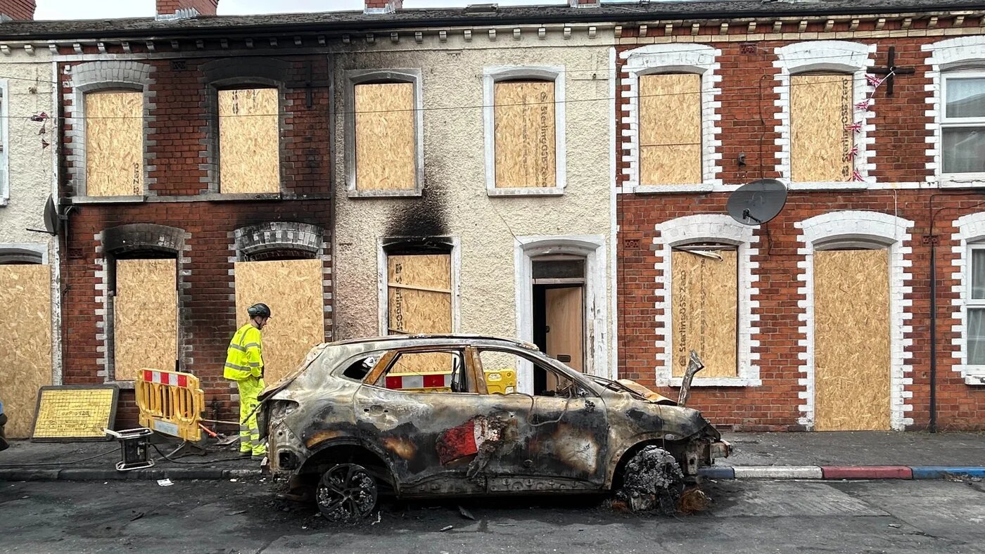 This picture shows a burned-out vehicle and home in Belfast on 11 June 2026 (Oscar Rickett/MEE)