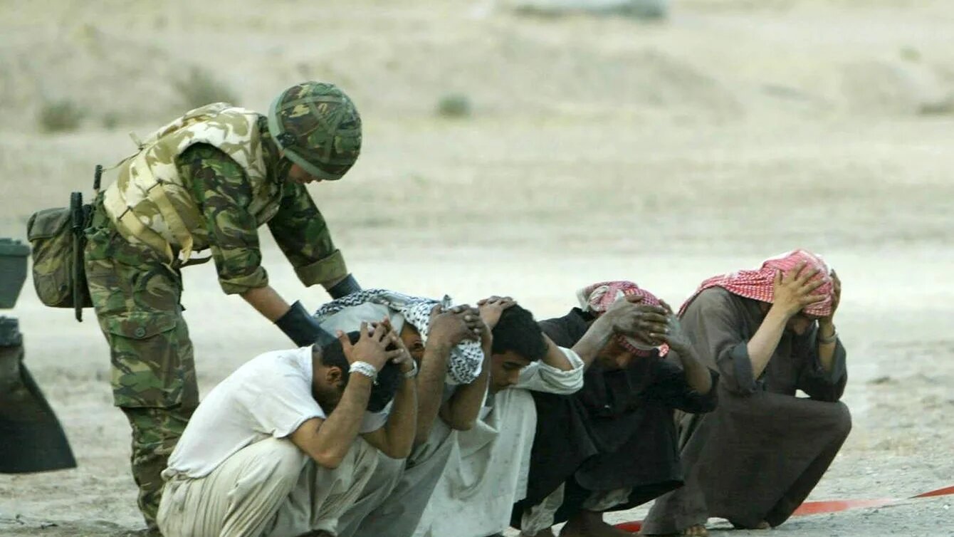A British soldier searches Iraqis at a checkpoint on the road to Basra in 2003