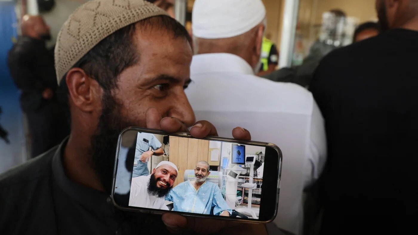 The brother of freed captive Kaid Alkadi shows a mobile phone picture of him with another brother, after his arrival for a check-up at the Soroka Medical Center in Beersheva in southern Israel on 27 August 2024 (AFP/Menahem Kahana)