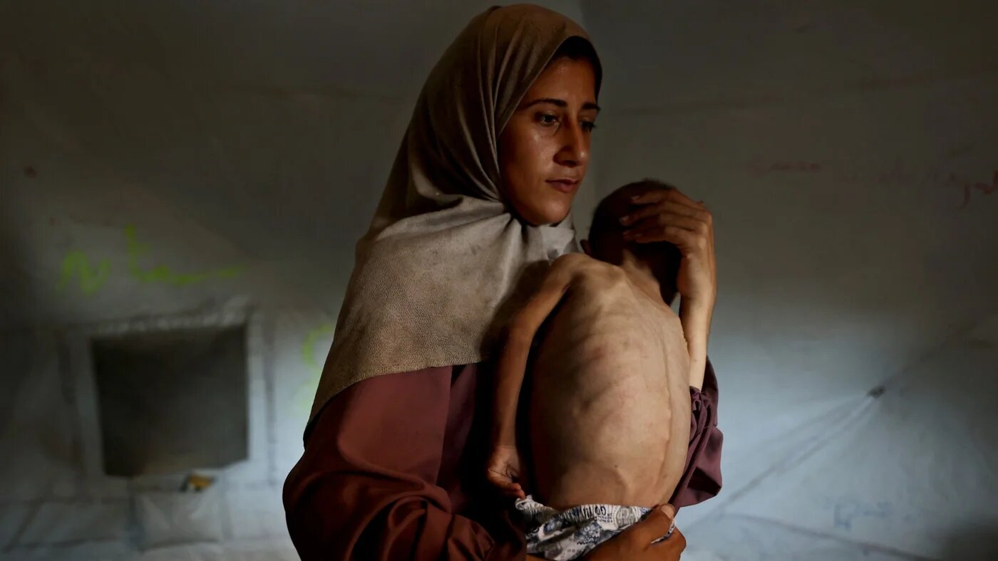 Hidaya, a 31-year-old Palestinian mother, carries her sick 18-month-old son Mohammed al-Mutawaq, inside their tent at the Al-Shati refugee camp, west of Gaza City, on 24 July 2025 (AFP/Omar al-Qattaa)